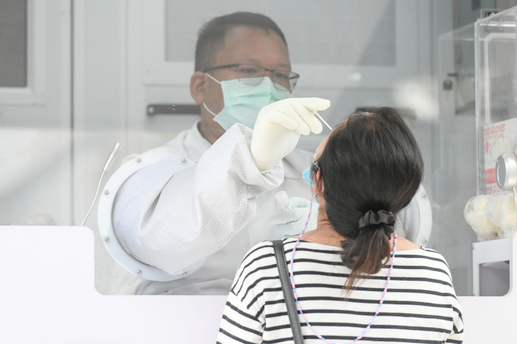 A health worker collects a nasal swab sample from a woman...