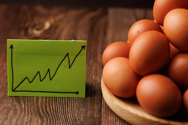 Wooden plate with eggs on dark wooden table with sticky notes presenting a rising price graph concept